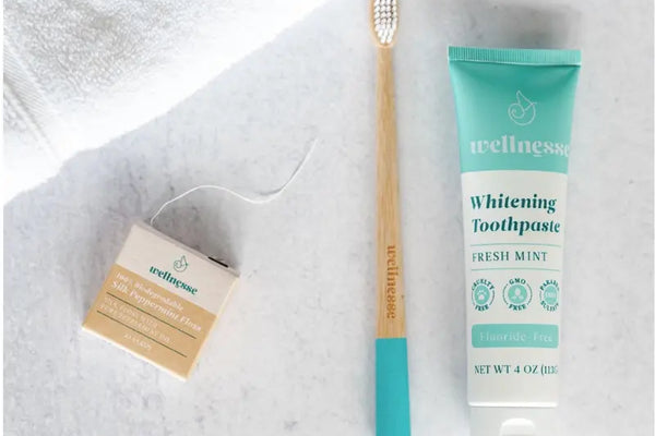 Best fluoride-free toothpaste paired with bamboo toothbrush and silk peppermint floss on white surface.