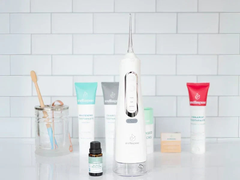 Non-fluoride toothpaste options displayed with oral care tools including a water flosser and bamboo toothbrush on a bathroom counter.