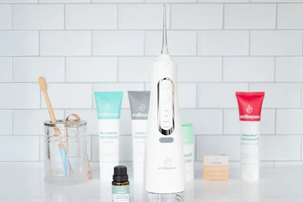 Non-fluoride toothpaste options displayed with oral care tools including a water flosser and bamboo toothbrush on a bathroom counter.