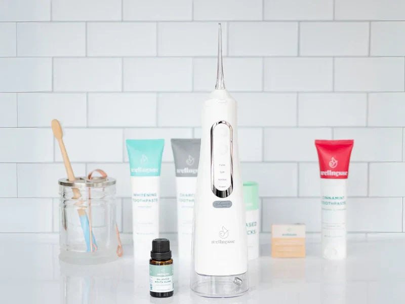 Non-fluoride toothpaste options displayed with oral care tools including a water flosser and bamboo toothbrush on a bathroom counter.