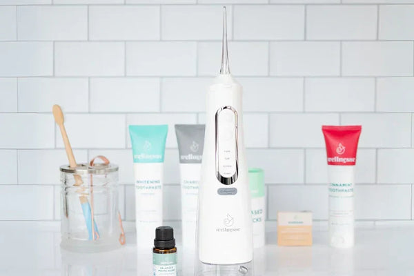 Non-fluoride toothpaste options displayed with oral care tools including a water flosser and bamboo toothbrush on a bathroom counter.