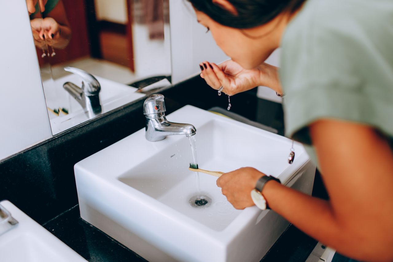 Woman brushing teeth at bathroom sink. 