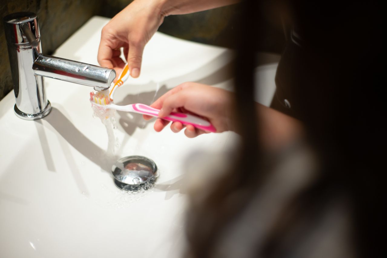 Hands rinsing toothbrush together at bathroom sink.