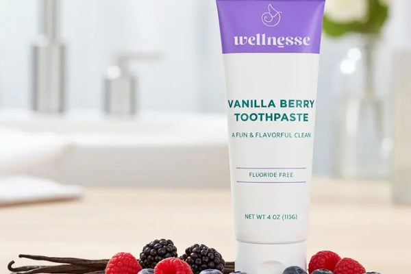 Remineralizing toothpaste tube of Wellnesse Vanilla Berry Toothpaste surrounded by fresh berries and vanilla beans
