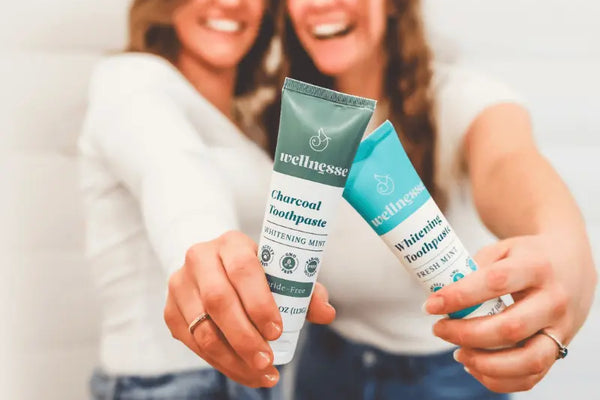Toothpaste for sensitive teeth held by two smiling women showing fluoride-free whitening and charcoal formulas.