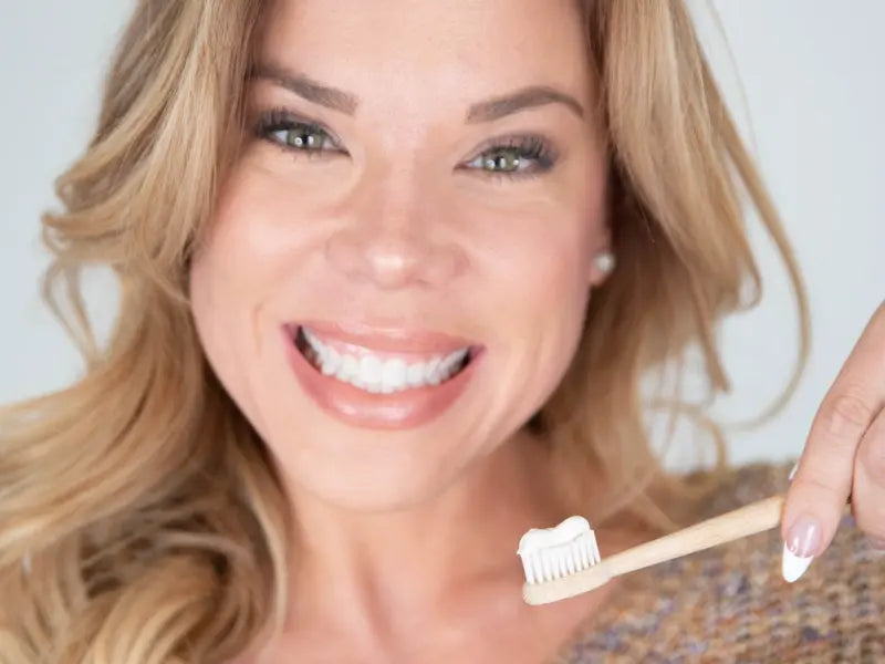 Toothpaste for sensitivity used by a smiling woman holding a bamboo toothbrush with paste