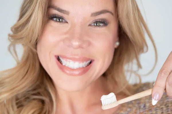 Toothpaste for sensitivity used by a smiling woman holding a bamboo toothbrush with paste