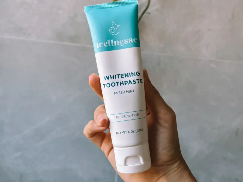 Toothpaste without fluoride shown in a hand, featuring Wellnesse Whitening Toothpaste