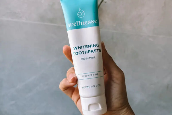 Toothpaste without fluoride shown in a hand, featuring Wellnesse Whitening Toothpaste