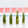 Strawberry healthy natural toothpaste in five fluoride-free tubes lined up with green foliage on a reflective white surface
