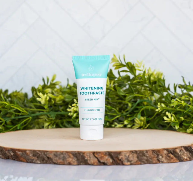 Travel size fluoride-free whitening toothpaste tube in fresh mint on a wood slice with greenery.