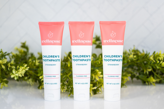 Strawberry healthy natural toothpaste in three fluoride-free tubes displayed in front of green leaves on a white surface
