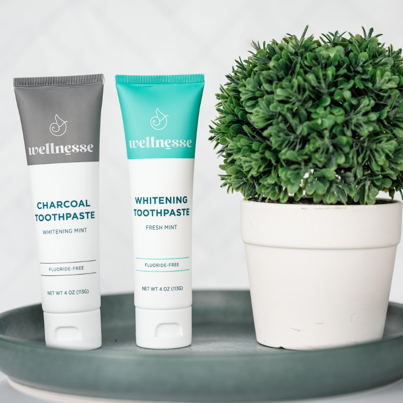 Charcoal and mint organic hydroxyapatite toothpaste tubes displayed alongside bamboo toothbrushes and natural dental floss on a wooden tray