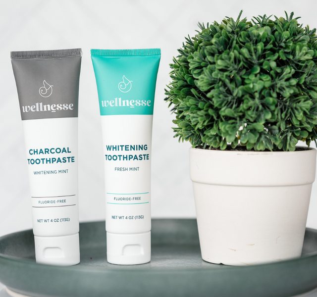 Charcoal and mint hydroxyapatite toothpaste tubes with bamboo toothbrushes and dental floss on a tray
