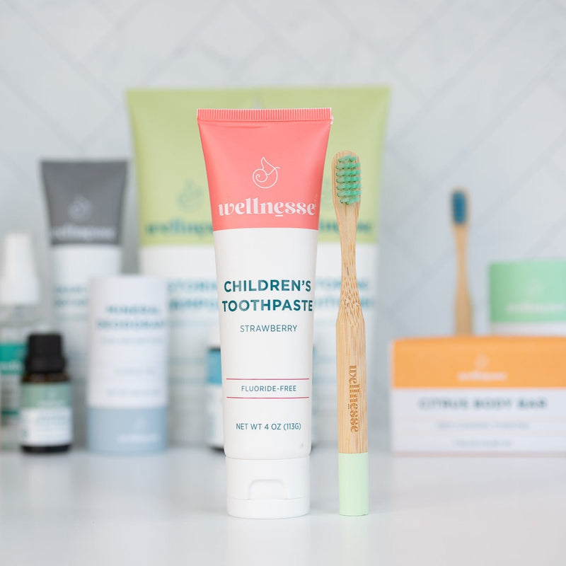 Wellnesse natural toothpaste for kids in strawberry alongside bamboo toothbrush and personal care products