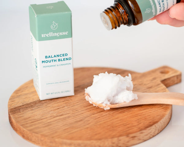 Concentrated mouthwash being dropped onto a spoonful of coconut oil next to Wellnesse Balanced Mouth Blend box.