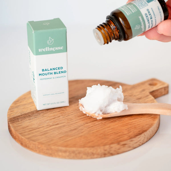 Concentrated mouthwash being dropped onto a spoonful of coconut oil next to Wellnesse Balanced Mouth Blend box.