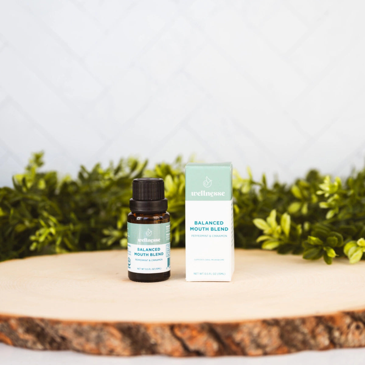 Concentrated mouthwash bottle and box labeled Balanced Mouth Blend with peppermint and cinnamon, displayed on wood with greenery.