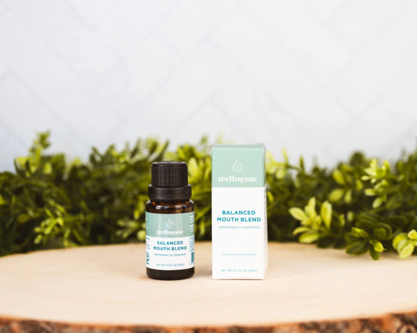 Concentrated mouthwash bottle and box labeled Balanced Mouth Blend with peppermint and cinnamon, displayed on wood with greenery.