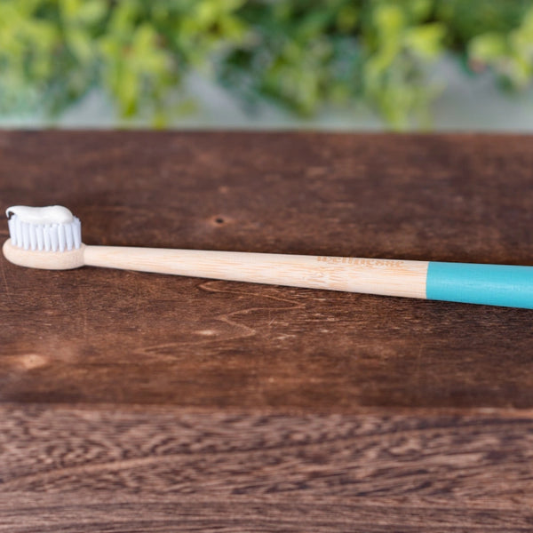Bamboo toothbrush with blue handle tip and toothpaste on bristles resting on a dark wooden box.