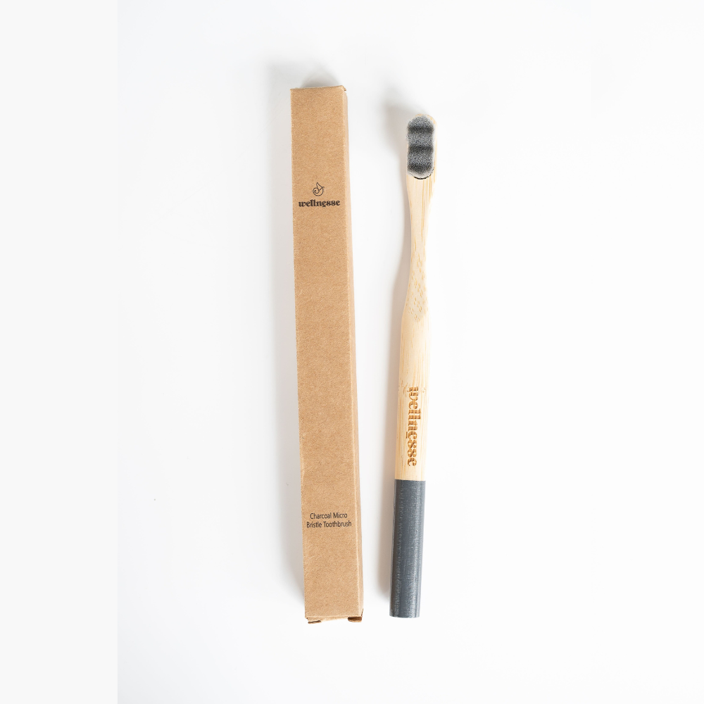 Charcoal toothbrush with black micro bristles and a bamboo handle, shown next to its eco-friendly cardboard packaging.