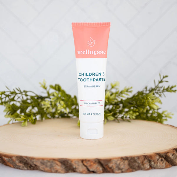 Wellnesse strawberry toothpaste for children, fluoride-free and displayed on a wood slice with greenery