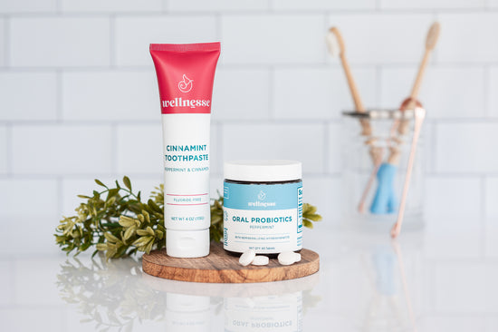 Cinnamon non toxic whitening toothpaste from Wellnesse paired with oral probiotics, displayed on a wooden tray with mint leaves.