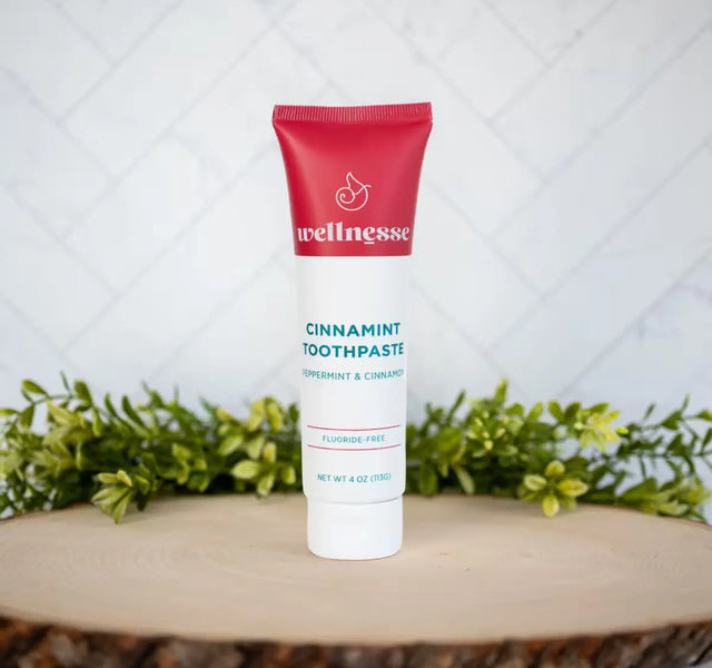 Wellnesse cinnamon toothpaste tube with red cap in peppermint and cinnamon flavor on a wood slice