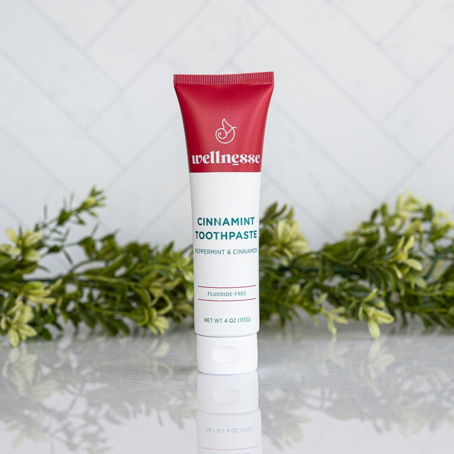 Cinnamon fluoride free toothpaste in a Wellnesse Cinnamint tube featuring peppermint and cinnamon, displayed with green foliage.