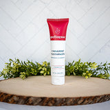 Cinnamon toothpaste by Wellnesse in a red and white tube, displayed upright on wood slice with greenery background.