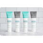 Lineup of four Wellnesse natural toothpaste tubes alternating fresh mint whitening and charcoal whitening mint flavors on a marble counter.