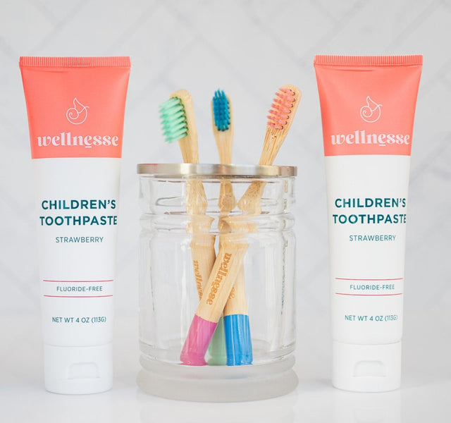 Child holding a Wellnesse kids bamboo toothbrush while brushing with strawberry toothpaste