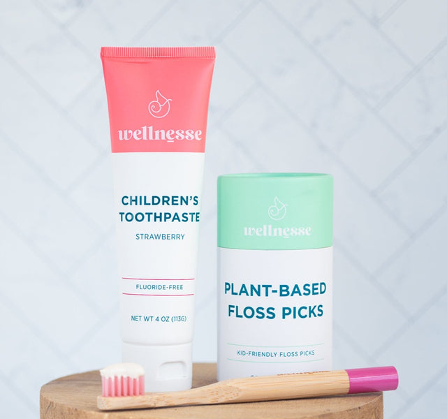 Wellnesse strawberry toothpaste paired with plant-based floss picks and a pink bamboo toothbrush