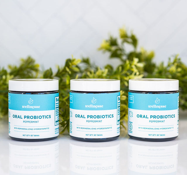 Three jars of Wellnesse peppermint oral probiotic mints with hydroxyapatite, arranged in front of greenery.