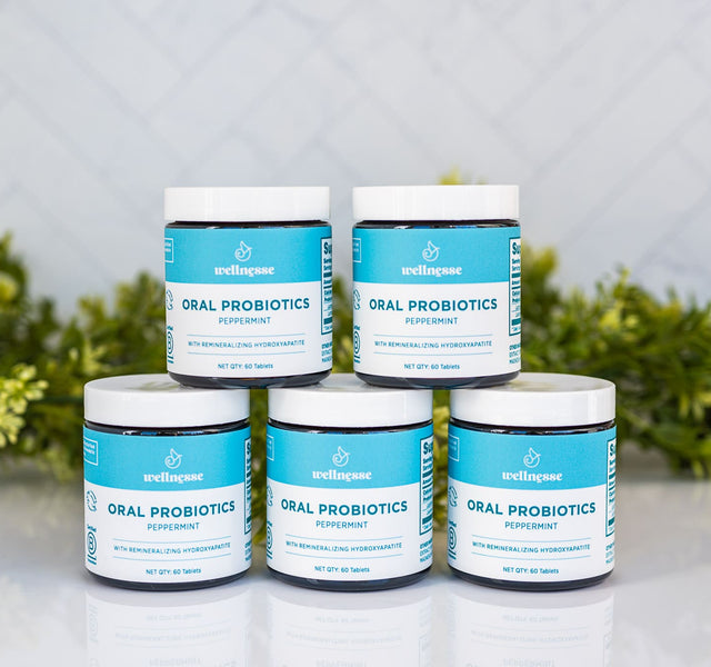 Five jars of Wellnesse peppermint oral probiotic mints stacked in a pyramid with greenery behind.