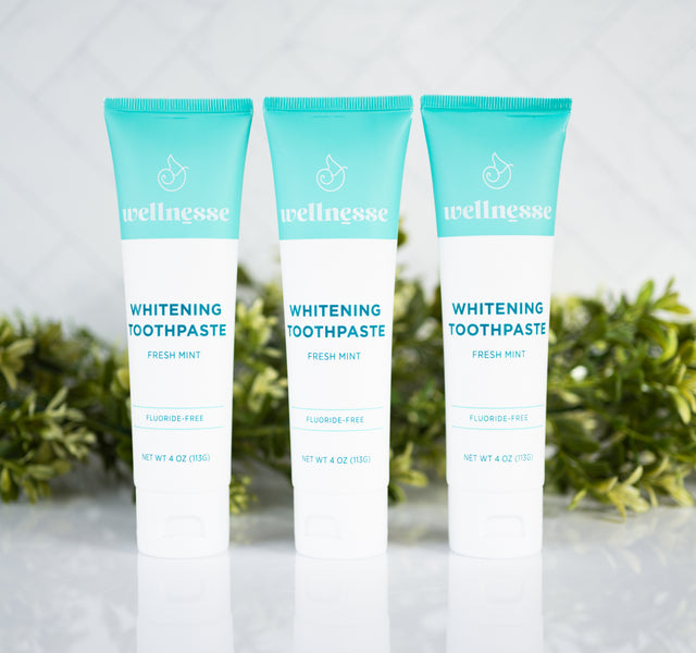 Fluoride-free mint whitening toothpaste trio from Wellnesse, featuring fresh mint flavor in teal and white tubes with a green botanical background.
