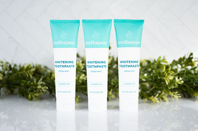 Mint whitening toothpaste trio from Wellnesse with fluoride-free formula, displayed in front of fresh greenery and a tiled backdrop.