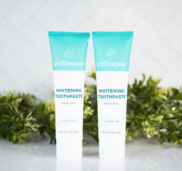 All natural whitening toothpaste tubes from Wellnesse, featuring fresh mint flavor and fluoride-free formula with green foliage background.