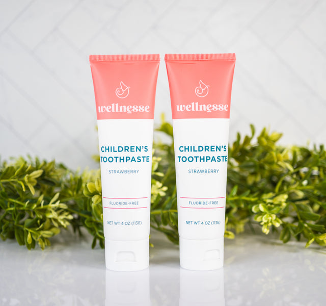 Strawberry healthy toothpaste without fluoride in two tubes displayed with green plants on a clean bathroom counter.