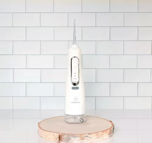 Wellnesse water flosser with multiple pressure settings on a wooden stand against a white tile background