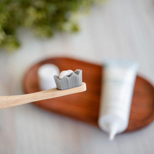 Wellnesse hydroxyapatite serum applied on a bamboo toothbrush with the product tube on a wooden tray
