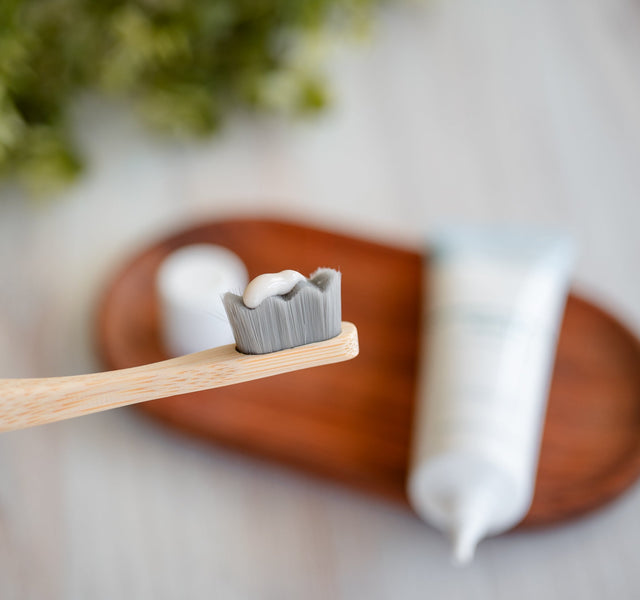 Wellnesse hydroxyapatite serum applied on a bamboo toothbrush with the product tube on a wooden tray