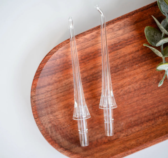 Wellnesse water flosser replacement nozzles on a dark wood tray with greenery nearby