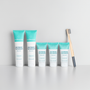 Fluoride-free whitening toothpaste by Wellnesse in five fresh mint tubes of two sizes lined up beside a bamboo charcoal toothbrush on a white surface.