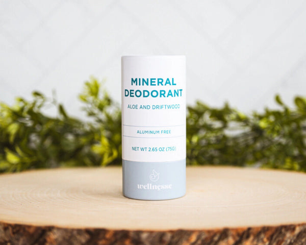Aluminum free deodorant labeled Mineral Deodorant with aloe and driftwood scent, displayed on a wooden slice with greenery.