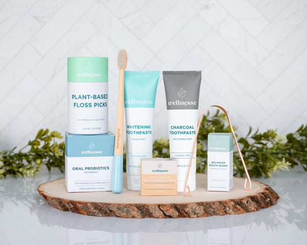 Oral care kit featuring Wellnesse products including toothpaste, floss, probiotics, floss picks, mouth blend, toothbrush, and tongue scraper.