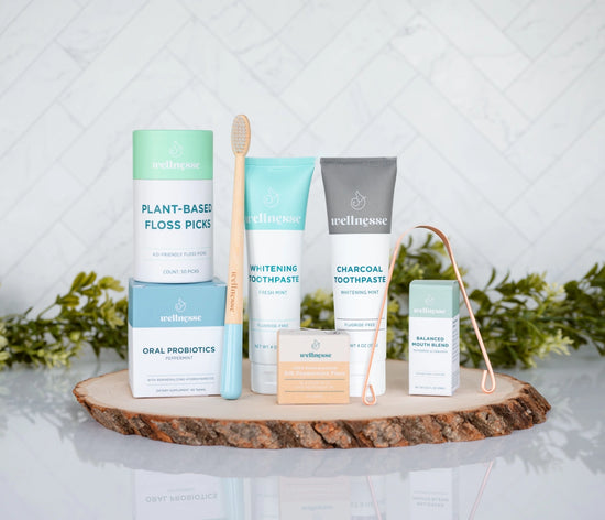 Oral care kit featuring Wellnesse products including toothpaste, floss, probiotics, floss picks, mouth blend, toothbrush, and tongue scraper.