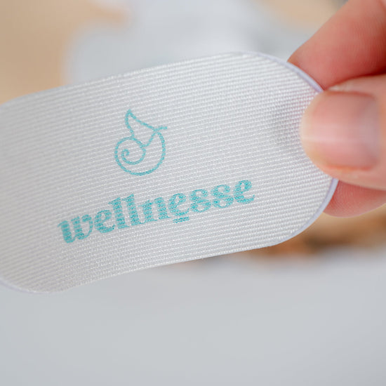 White mouth tape with 'wellnesse' branding held by a hand on a light background