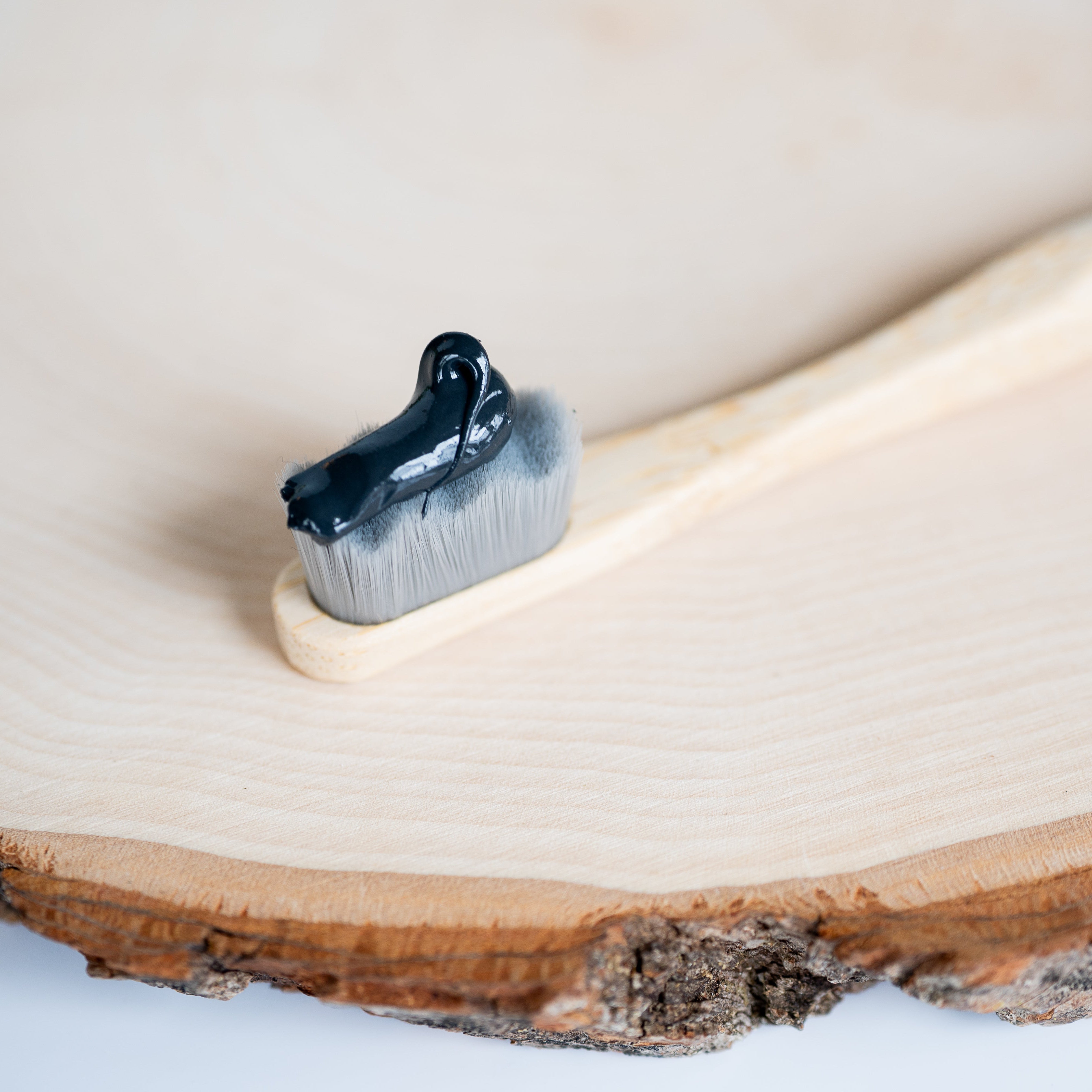 Charcoal toothpaste applied on a soft-bristled bamboo toothbrush, resting on a natural wood slice background.
