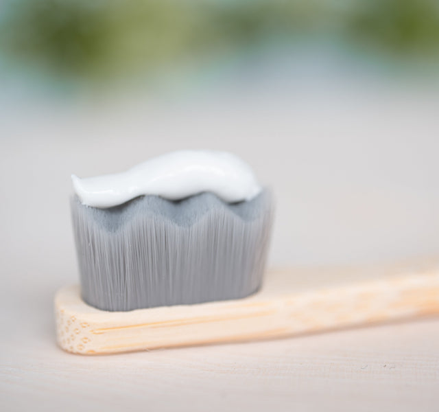 Fluoride-free toothpaste on a bamboo toothbrush head shown in close-up macro detail with a soft blurred background.